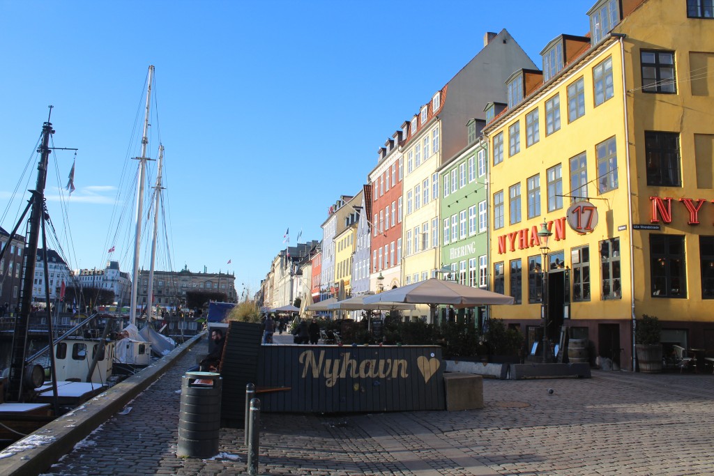 Nyhavn sunny side with outdoor restaurants in former store houses close to wharf. View to concrete barrier covered with bench, floerrs and climbing for children